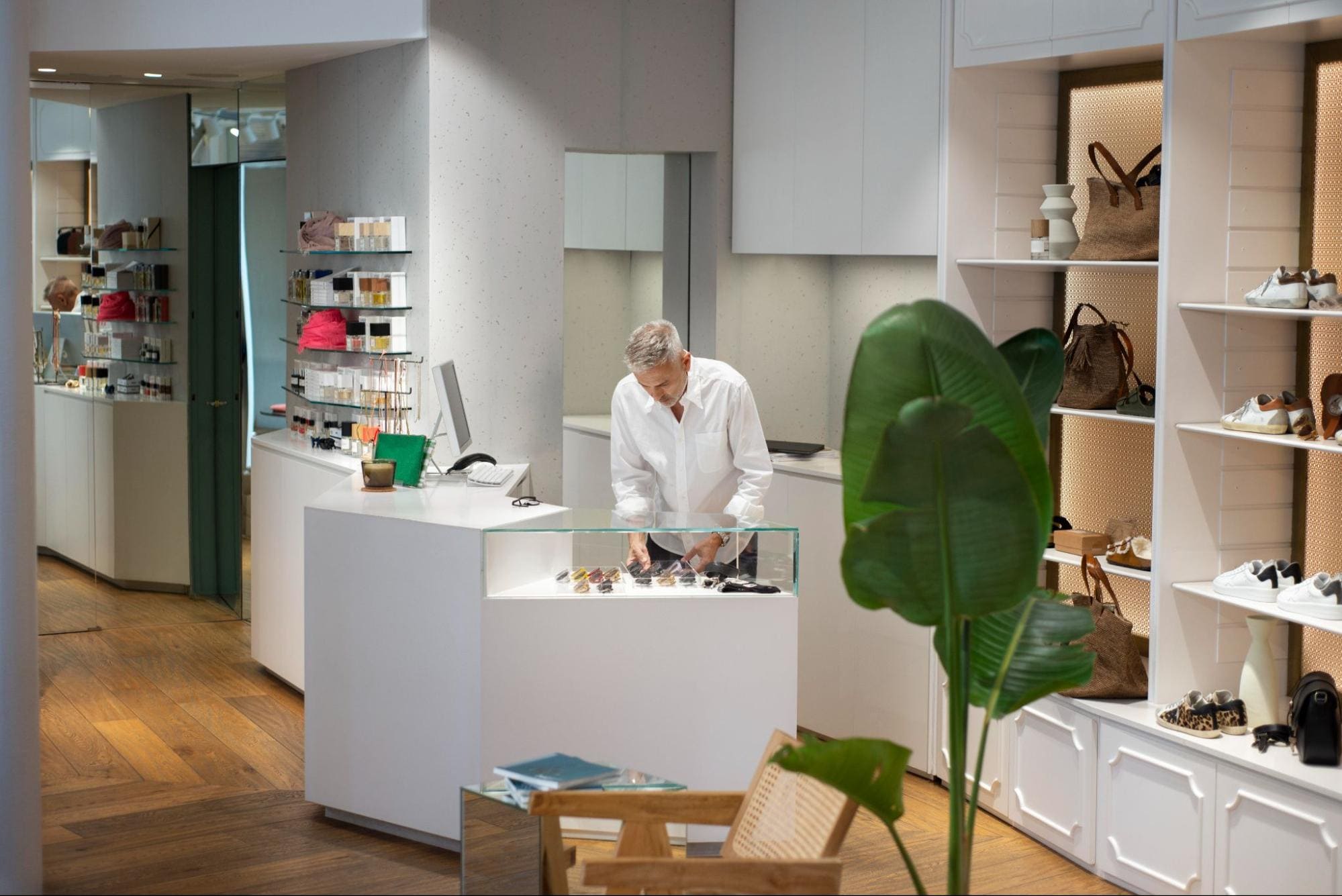 A store owner arranging items in a glass display case surrounded by shelves of handbags, shoes, and accessories in a boutique retail space